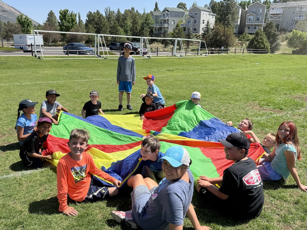 A picture of kids at the park with a large kite at the Unlocked Potential back to school fun bash camp in Flagstaff, AZ